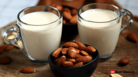 Two glasses of almond milk beside a bowl of almonds, with a blurred background featuring more almonds